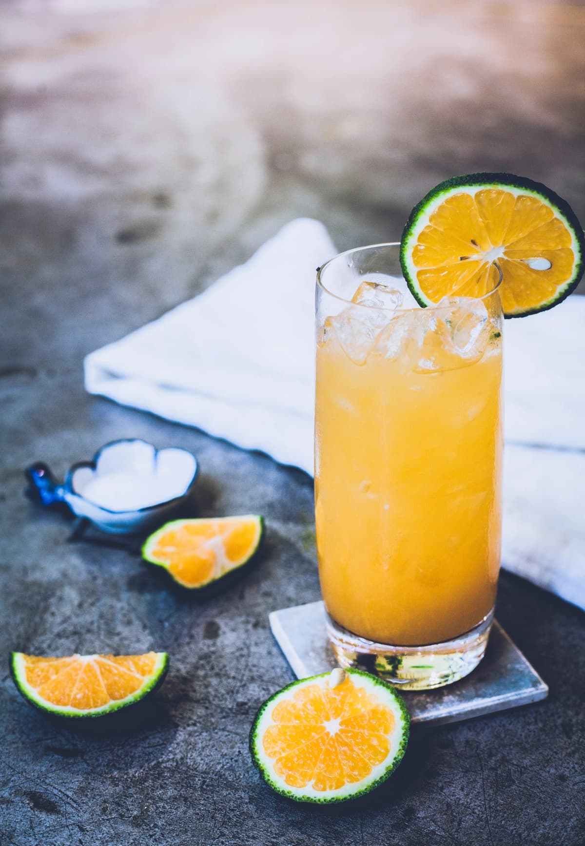 Orange and lime cocktail with a slice of orange, served on the rocks, garnished with lemon and lemon juice on the glass.